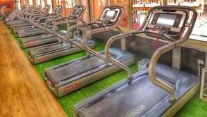 Une rangée de tapis de course dans une salle de sport, avec un plancher en bois et une moquette verte, de grandes fenêtres et un plafond en bois.