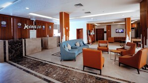 Un hall d’hôtel comprenant un comptoir d’accueil, un espace salon et un écran de télévision.