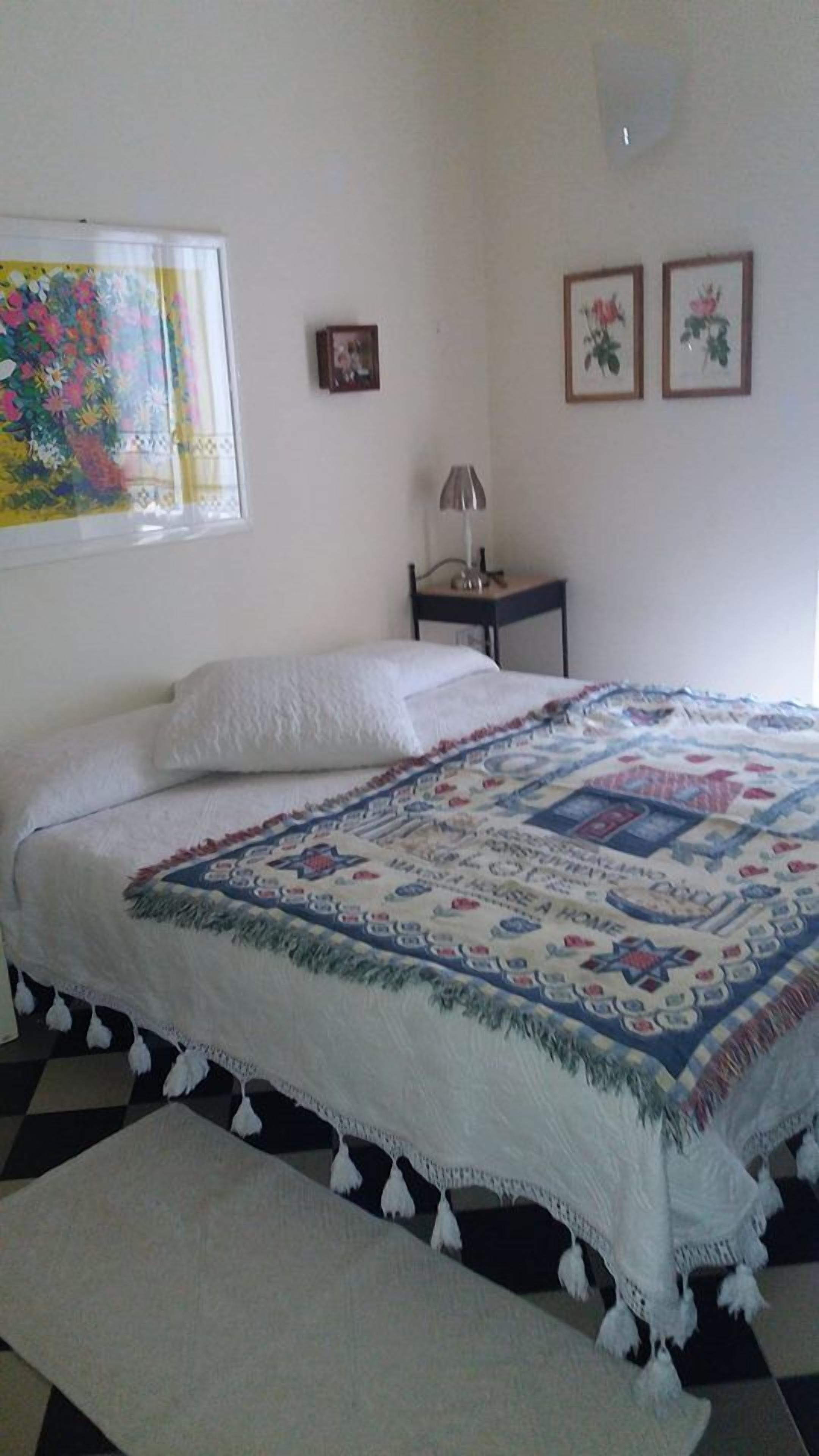 A bedroom with a bed, a nightstand, a lamp, and a window with a floral curtain.