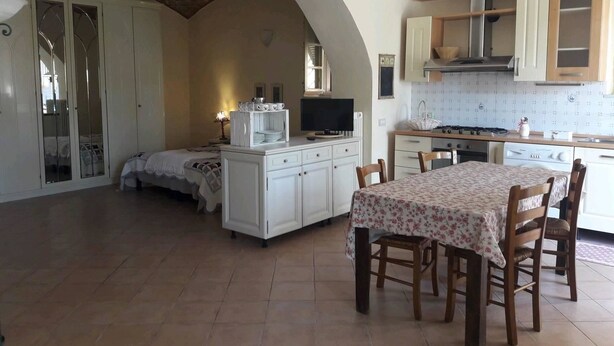 A spacious room with a dining area, a kitchen, and a bedroom with a large arched doorway. - I Fiori di Miranda (Casarza Ligure)