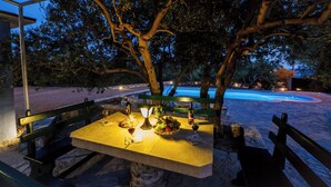 An outdoor dining area with a table set for two, under a tree, overlooking a swimming pool. - Luxury villa complex Pendolino with heated pool and jacuzzi (Kastela)