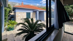 A view from inside a room with a large window overlooking a small building with a red roof and stone walls. - Luxury villa complex Pendolino with heated pool and jacuzzi (Kastela)