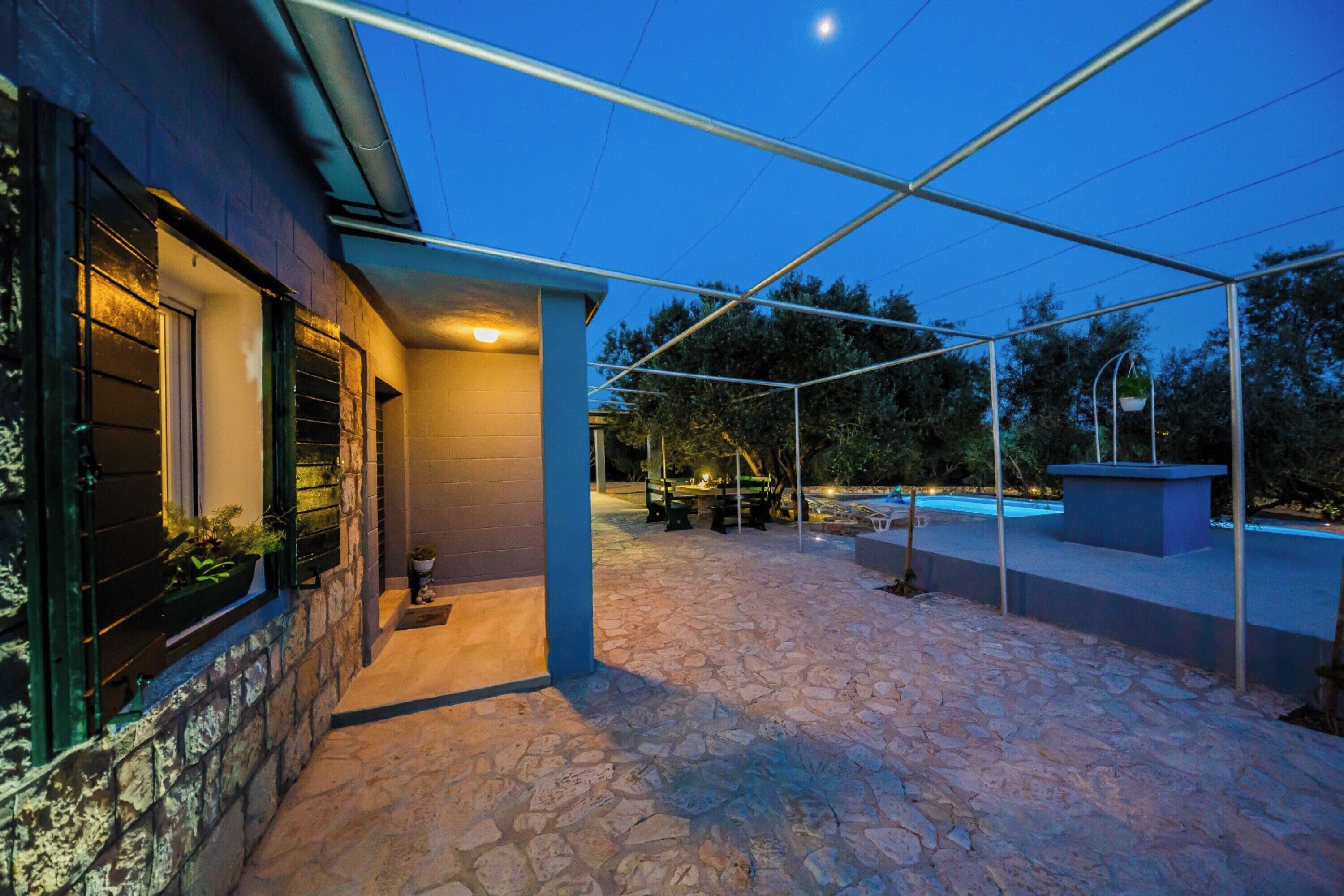 Eine gepflasterte Terrasse mit Pool, Sitzgelegenheit im Freien und einem überdachten Bereich mit Blick auf den Pool.