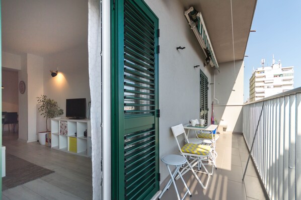 Ein Balkon mit Fernseher, einer Pflanze und einem Essbereich mit Stühlen und Tisch.