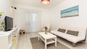 A modern living room with a white sofa, a coffee table, a TV on a white stand, a red pendant light, and a painting of a beach scene. - Exclusive apartment in center with amazing view! (Split)