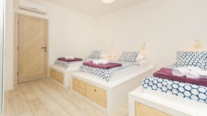 A modern bedroom with two beds, a wooden door, an air conditioning unit, and a hanging light fixture. - Exclusive apartment in center with amazing view! (Split)