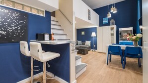 A modern kitchen with a bar area, a staircase, and a dining space with blue chairs. - happy home Budapest BLUE (Budapest)