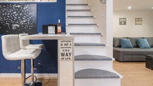 A modern living room with a white bar stool, a staircase, and a sofa with blue cushions. - happy home Budapest BLUE (Budapest)