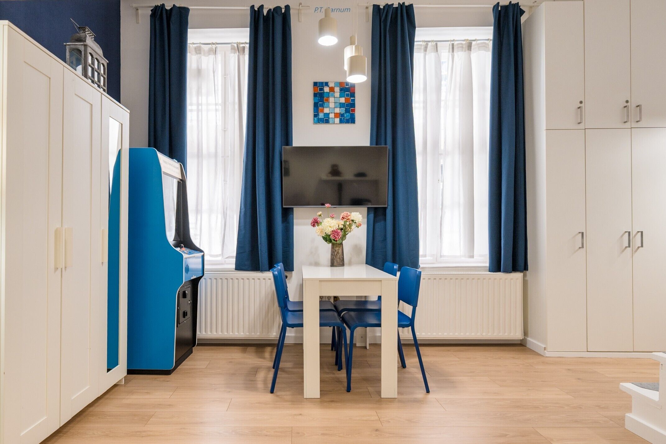 A room with a white table, blue chairs, a TV, and a radiator.