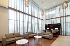 Eine moderne Hotelhalle mit großen Fenstern, Sofas, einem Couchtisch und einem Schreibtisch mit Computern.