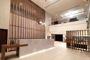 Eine moderne Lobby mit einer Rezeption, einer hohen Decke mit eingelassener Beleuchtung und einer Wand mit Musterung.