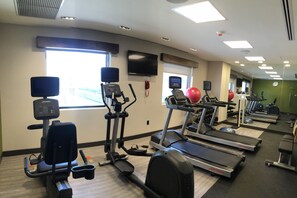 Une salle de sport équipée de tapis de course, de vélos elliptiques et de ballons d’exercice.