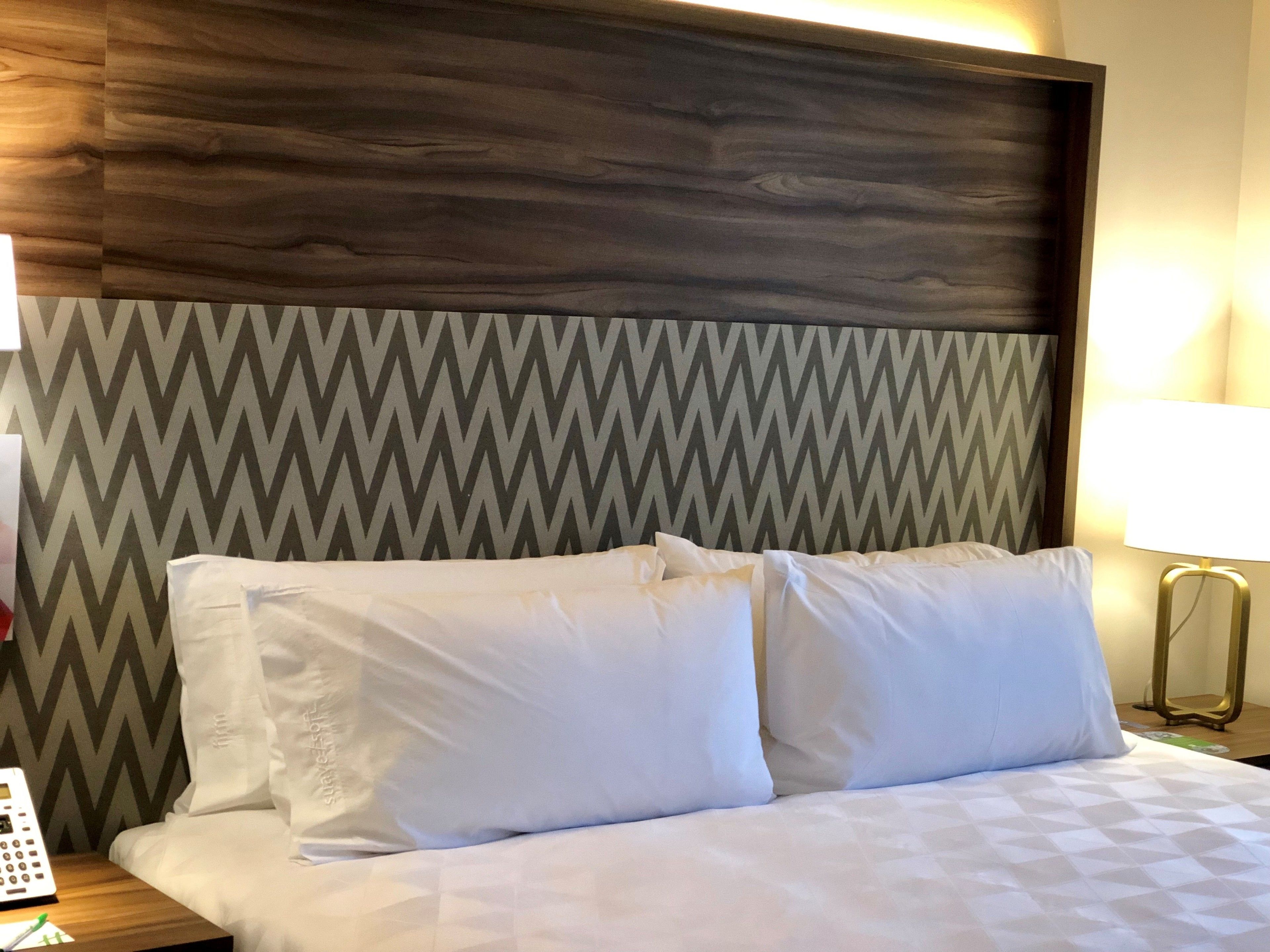 A hotel room with a bed, a nightstand, a lamp, and a wall with a chevron pattern.