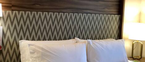 A hotel room with a bed, a nightstand, a lamp, and a wall with a chevron pattern.