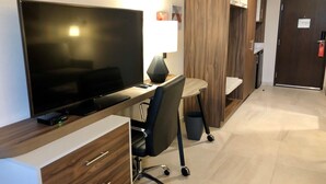 Quarto de hotel moderno com televisão de tela plana, uma escrivaninha com luminária, uma cadeira e um guarda-roupa.