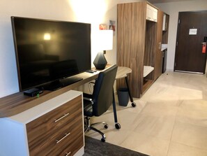 Une chambre d’hôtel moderne équipée d’une télévision à écran plat, d’un bureau avec une lampe, d’une chaise et d’une armoire.