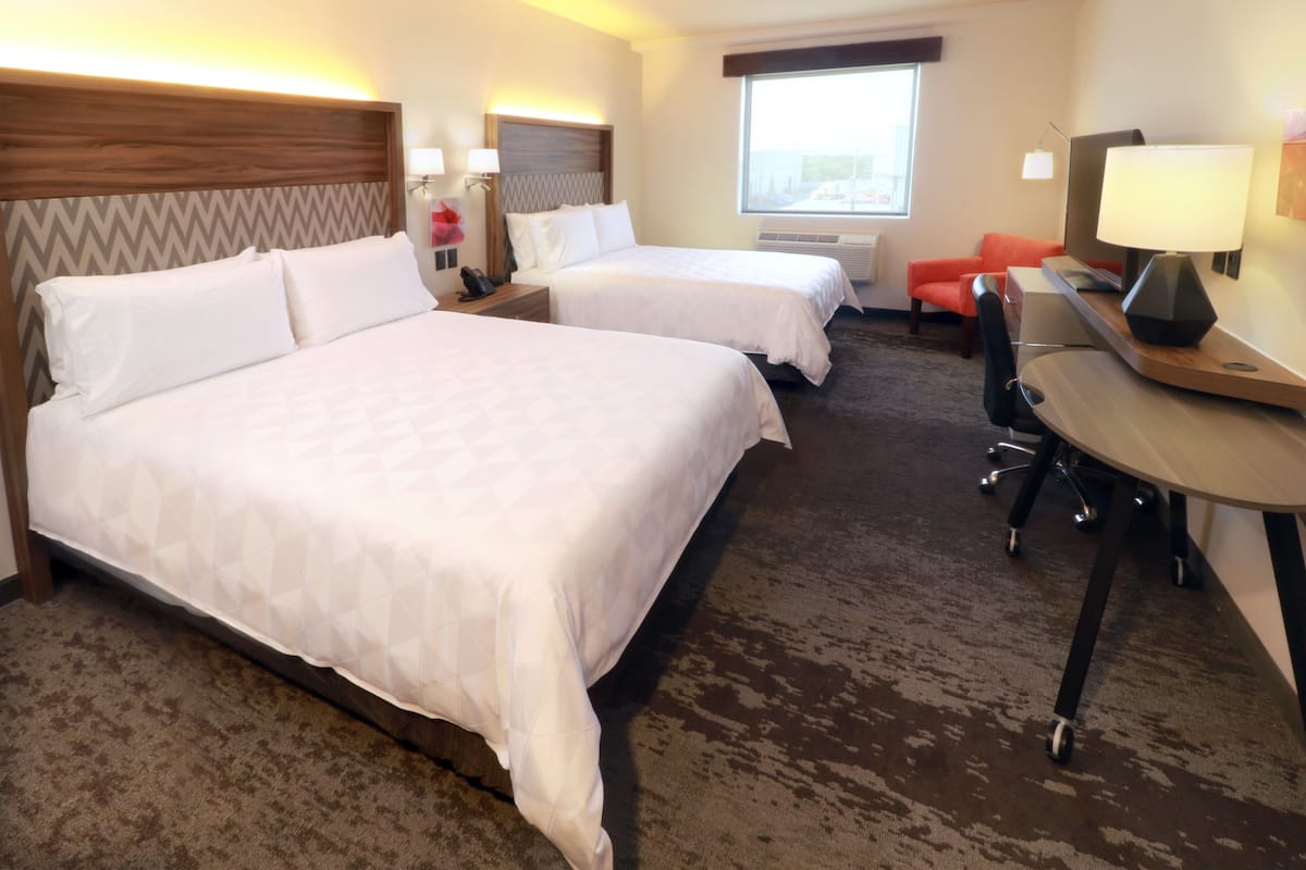 A hotel room with two beds, a desk, a chair, a TV, and a window.