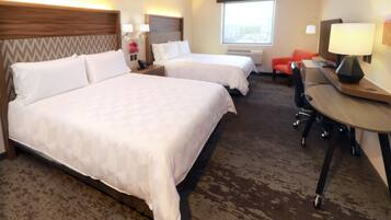 A hotel room with two beds, a desk, a chair, a TV, and a window.