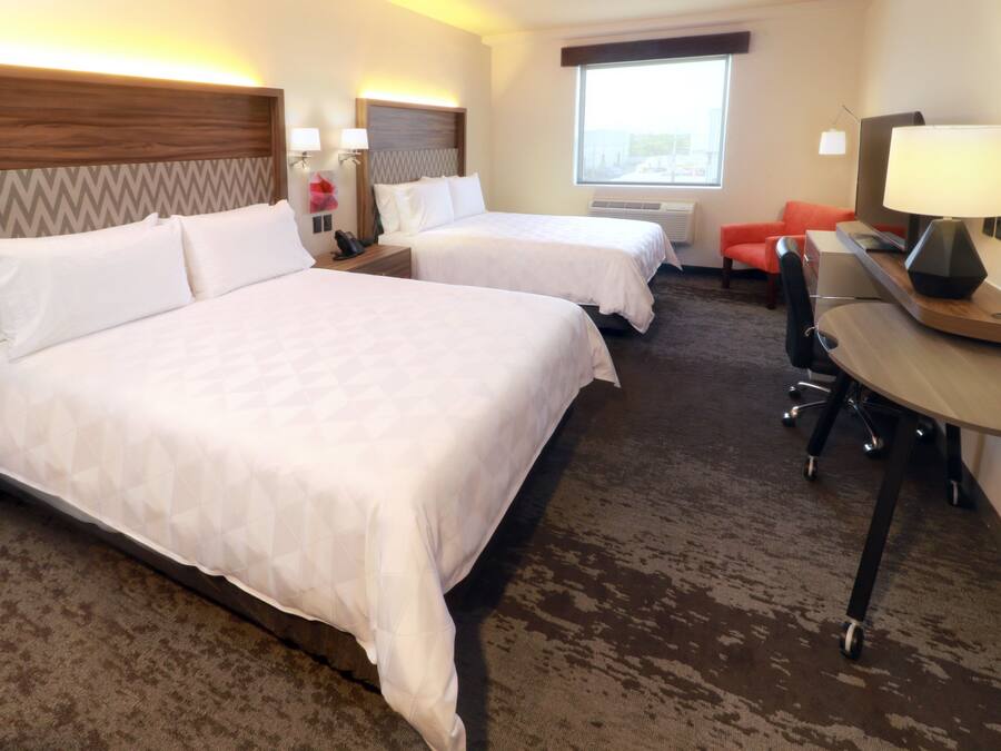 A hotel room with two beds, a desk, a chair, a TV, and a window.