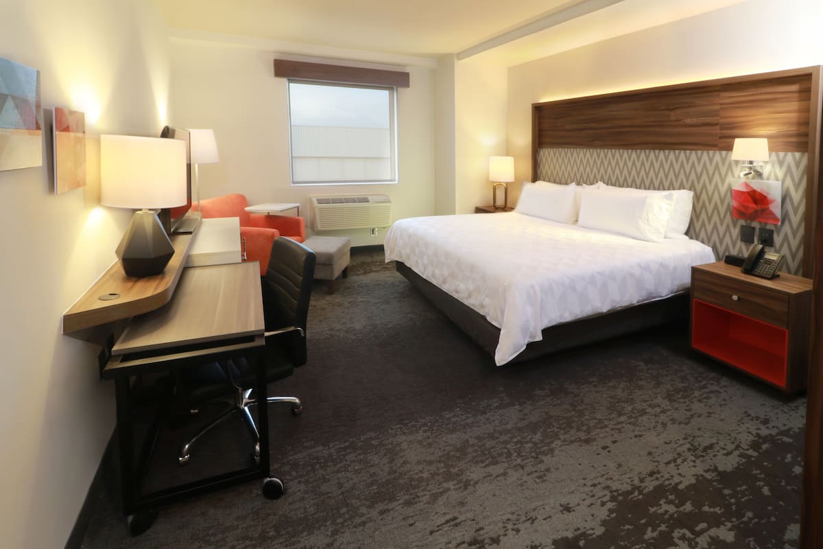 A hotel room with a bed, desk, chair, and a small seating area.
