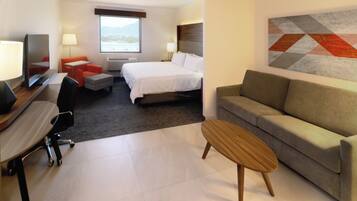 Habitación de hotel con cama, sofá, escritorio con silla, televisor y ventana con vistas.