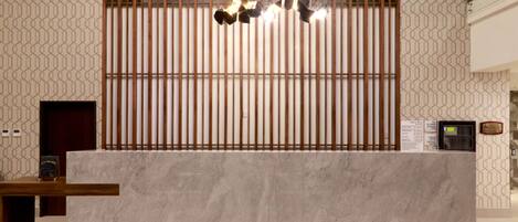 A reception desk with a marble top, vertical wooden slats, and a hanging light fixture.
