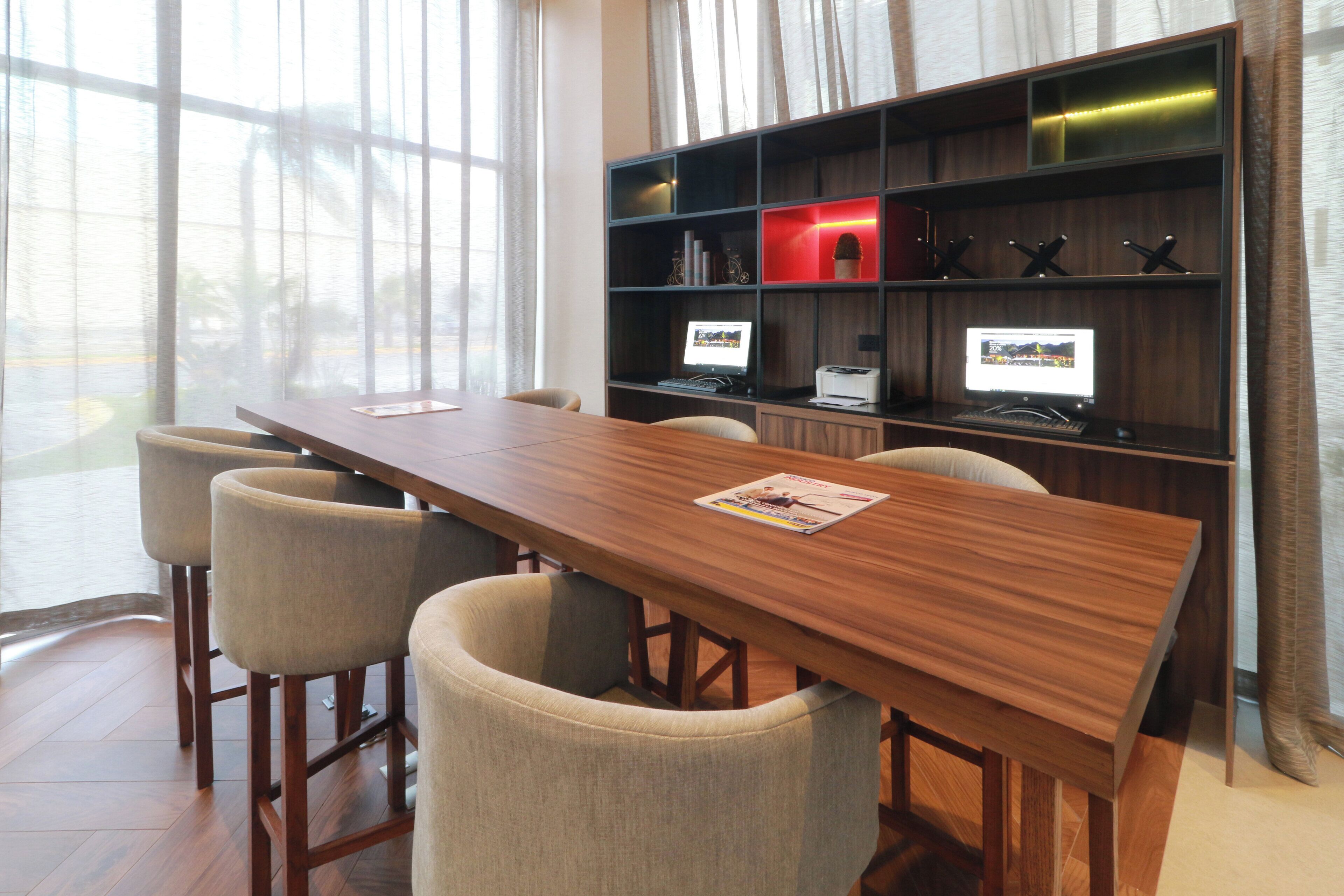 A conference room with a long wooden table, four chairs, and two desktop computers.