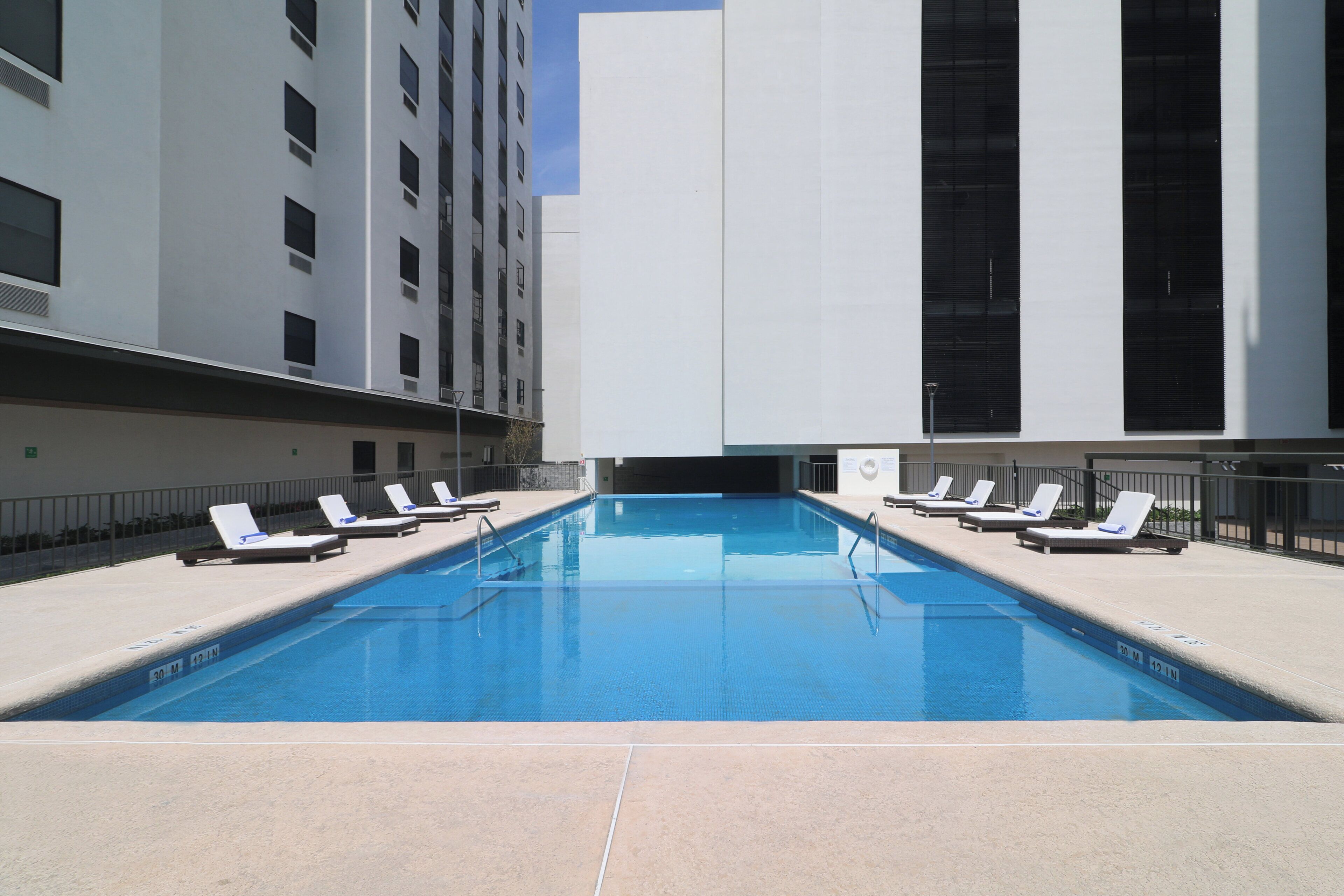 A swimming pool with lounge chairs and a modern building in the background.