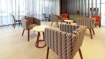 A modern hotel lobby with patterned armchairs, a round table, and a reception desk.