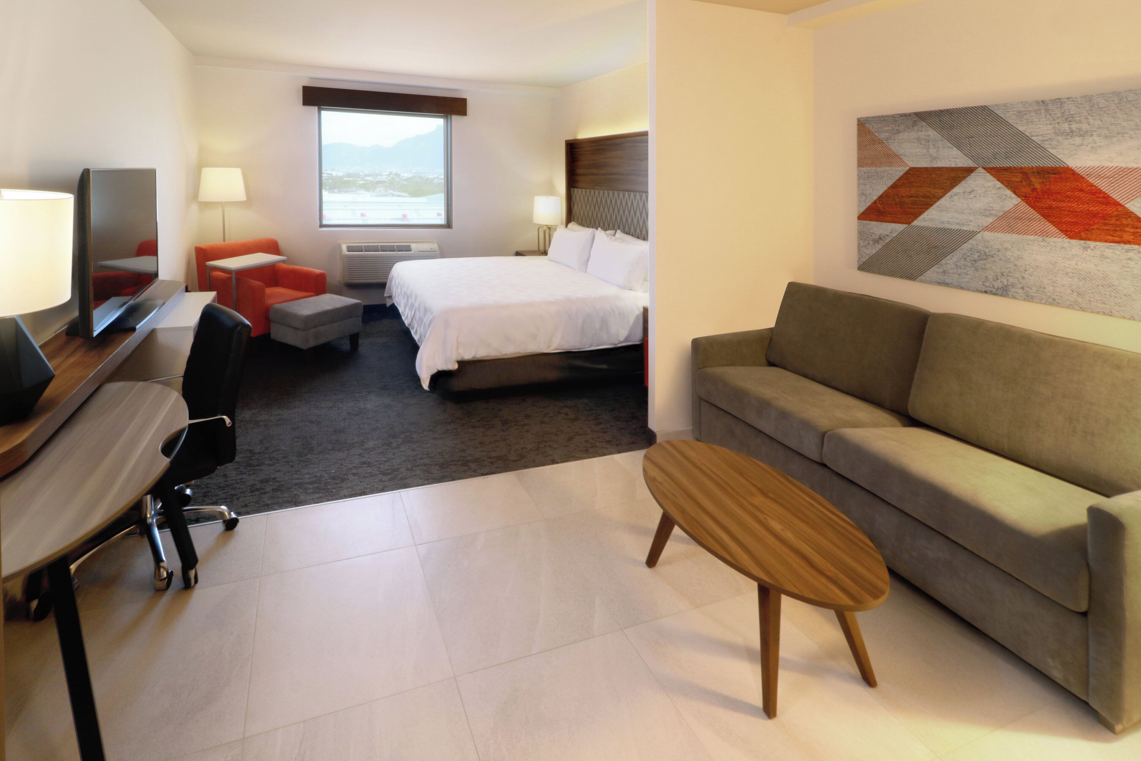 A hotel room with a bed, a sofa, a desk with a chair, a TV, and a window with a view.