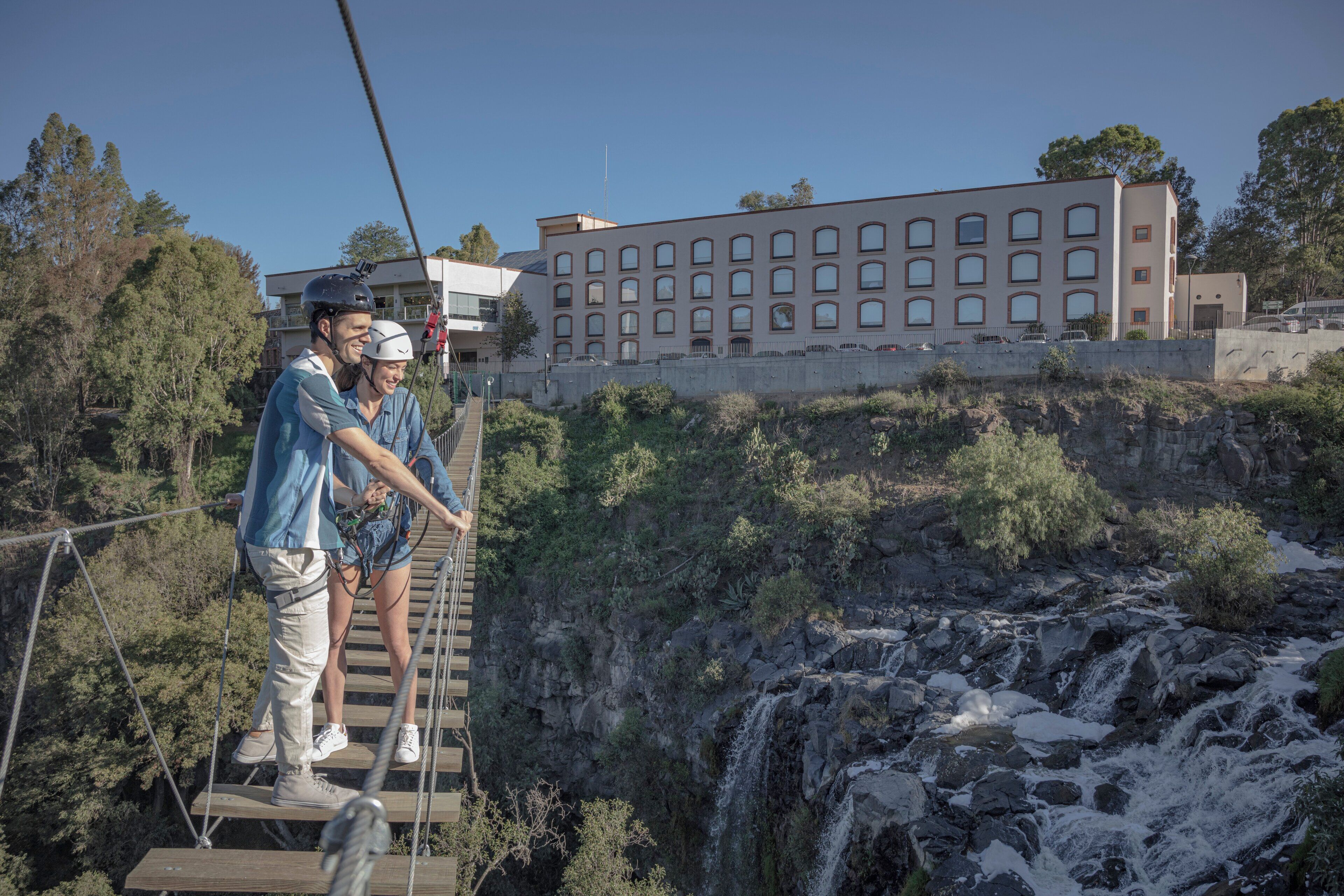 A suspension bridge with a waterfall in the background.