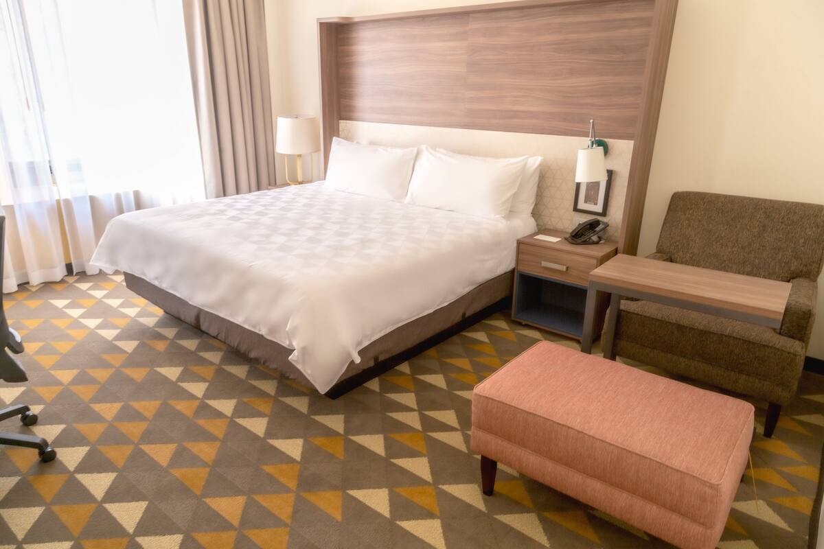 A hotel room with a large bed, a desk, a chair, and a small table.