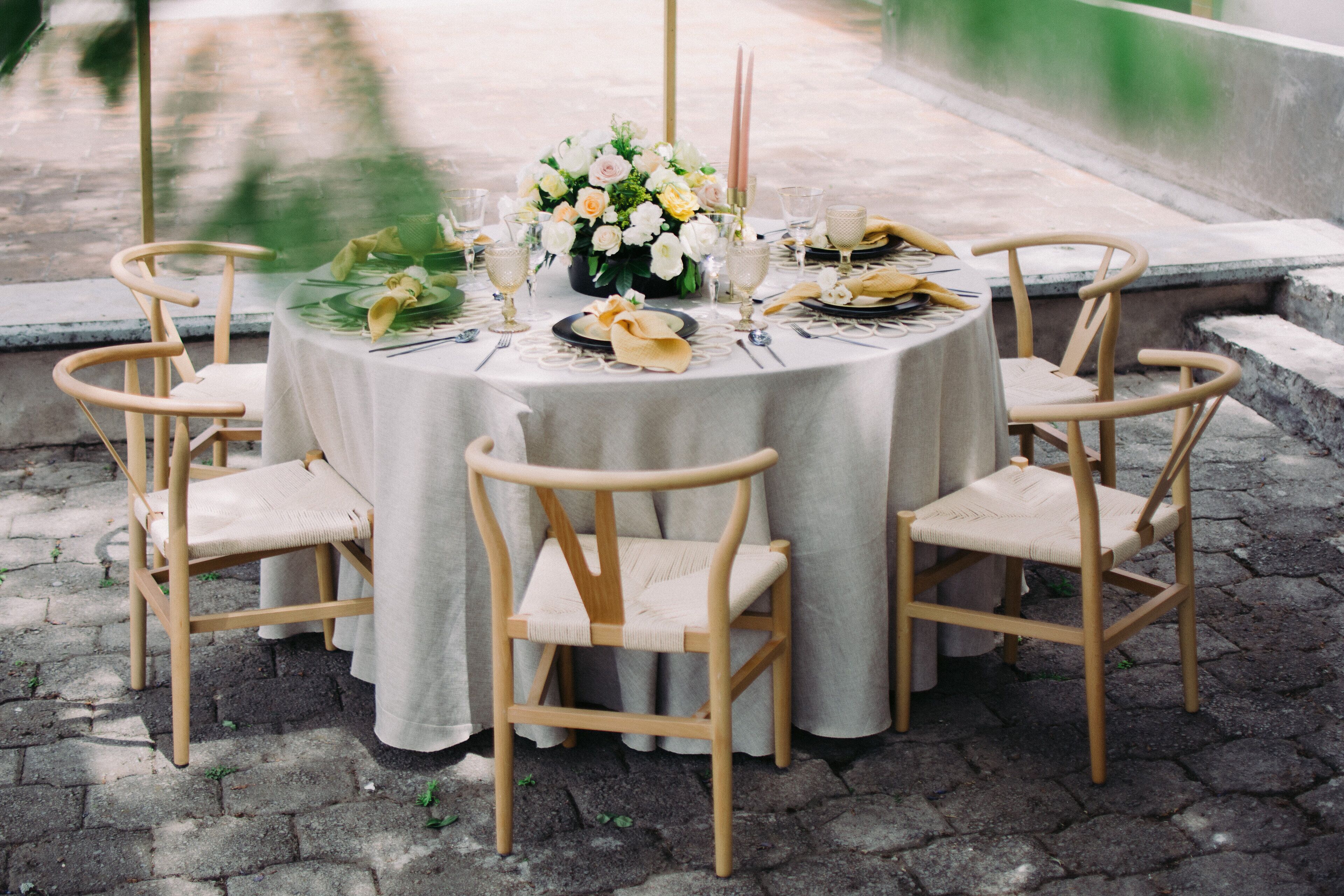 Une table ronde recouverte d’une nappe blanche, entourée de six chaises en bois dotées d’assises rembourrées.