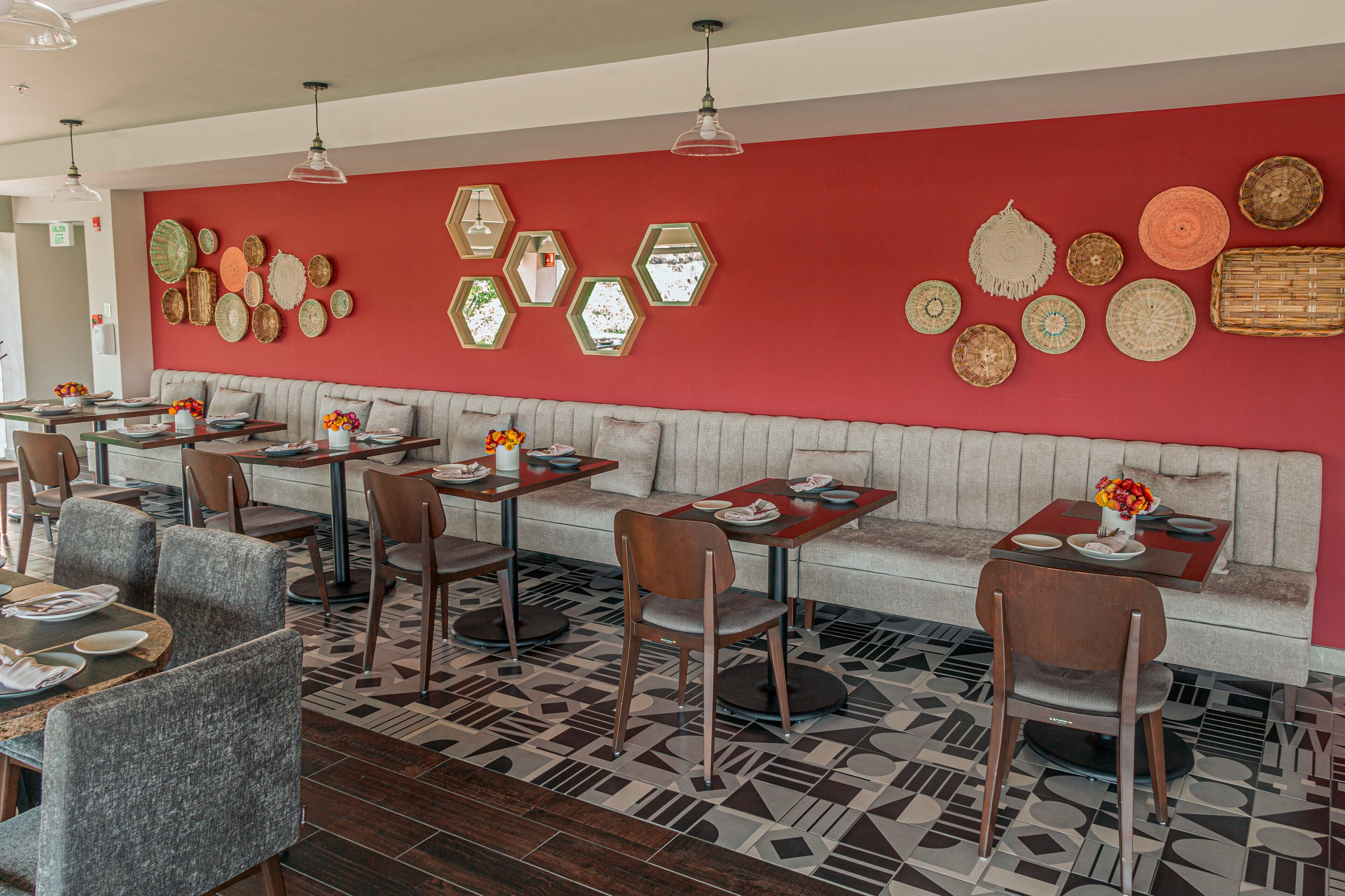 A restaurant with a red wall, hexagonal mirrors, and a patterned floor. Tables and chairs are arranged for dining.