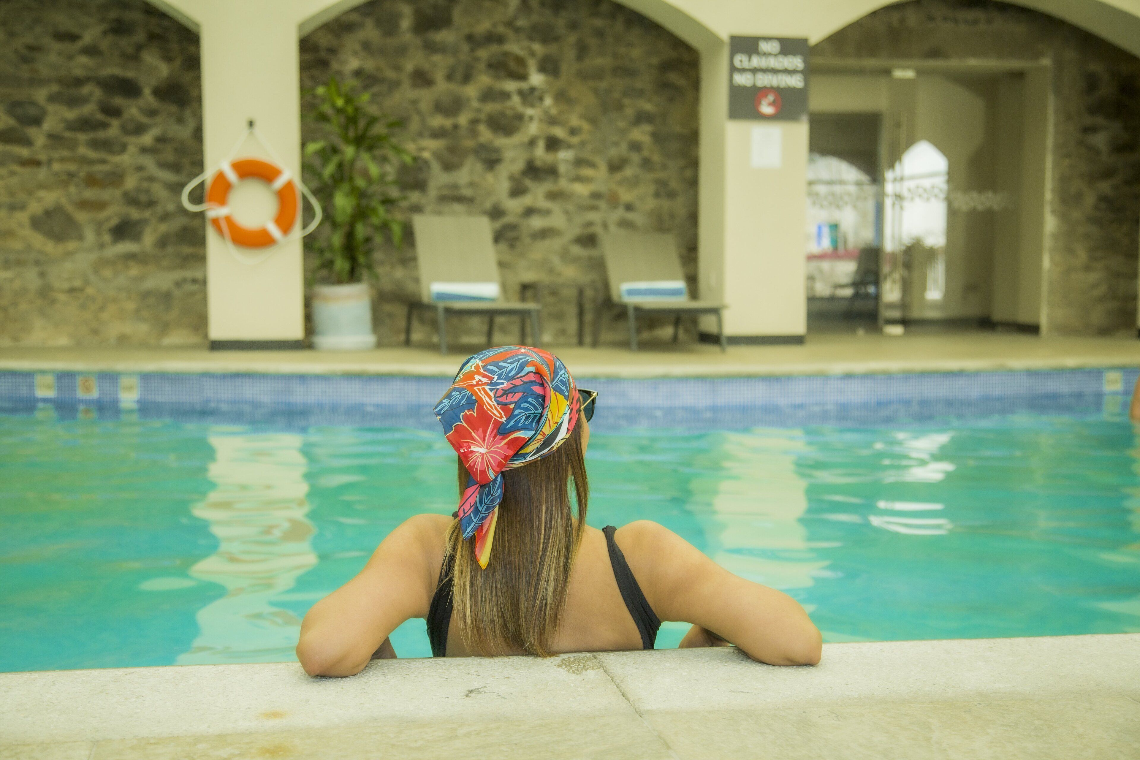 A pool area with a stone wall, lounge chairs, and a lifebuoy.