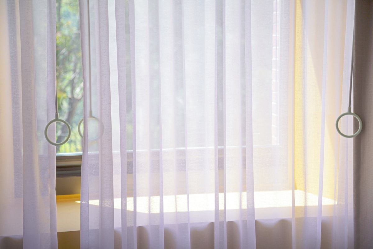 Janela com cortinas leves e luminária com anel.