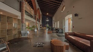A spacious lobby with high ceilings, exposed brick arches, and a mix of seating areas including a leather couch and a wooden table. - Holiday Inn Tlaxcala by IHG (Yauhquemehcan)