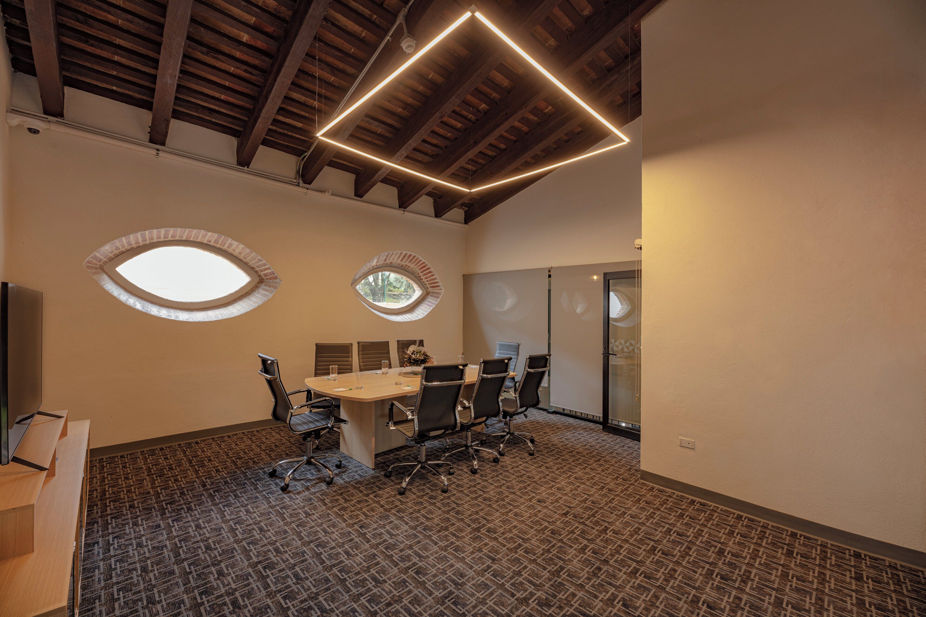 A conference room with a high ceiling, two skylights, a long table with chairs, and a carpeted floor.