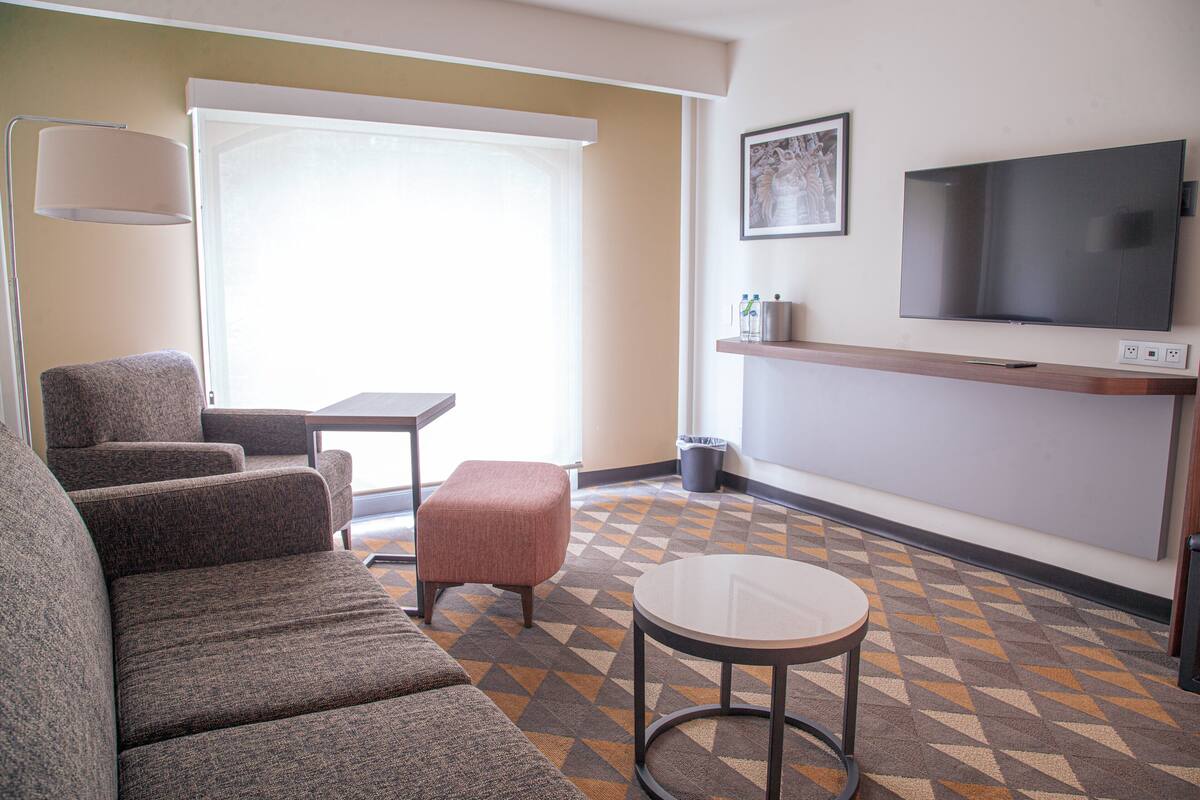 A hotel room with a sofa set, a small table, a TV mounted on the wall, and a patterned floor.
