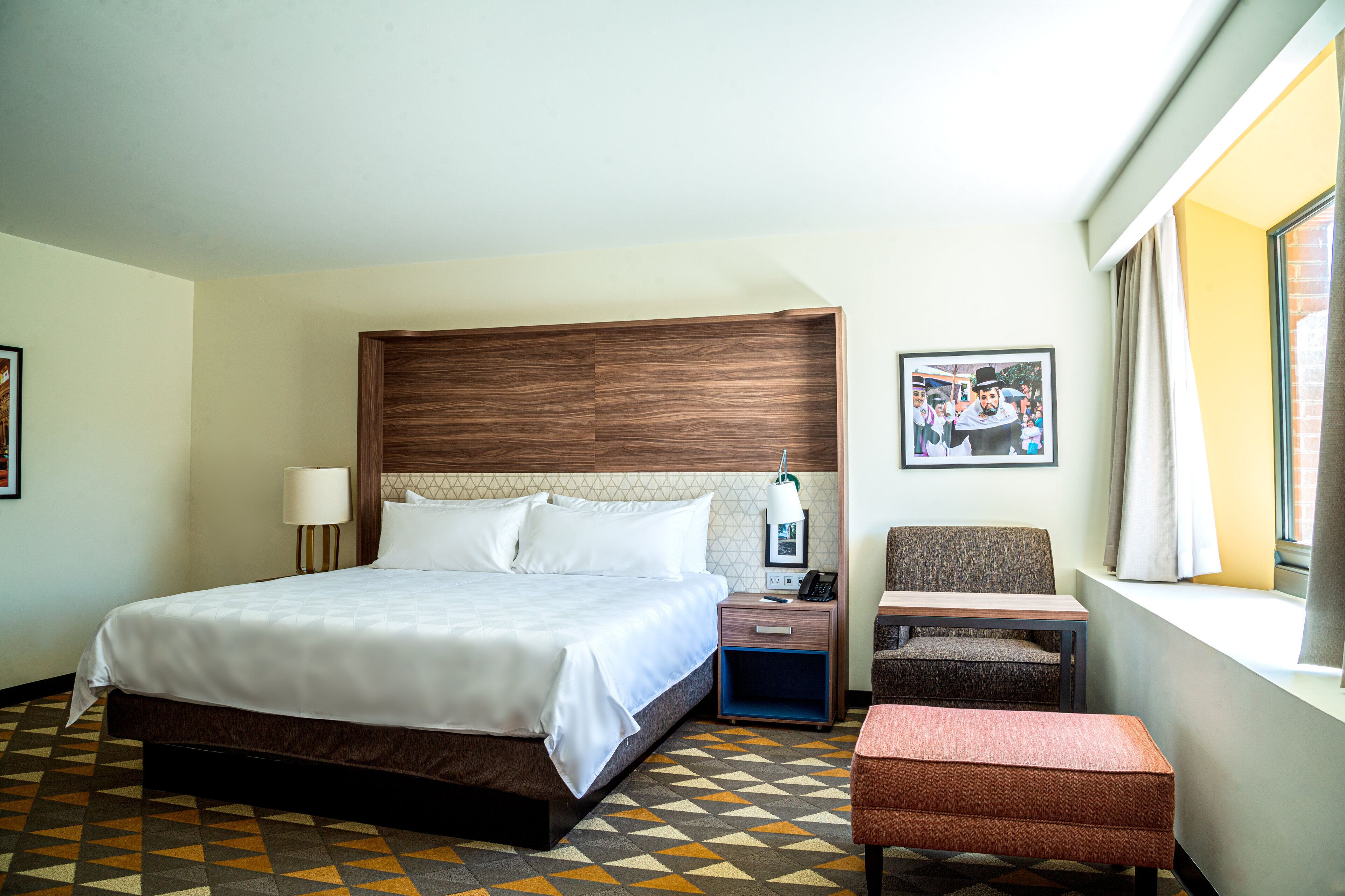 A hotel room with a large bed, a bedside table with a lamp, a chair, and a small table.