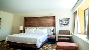 A hotel room with a large bed, a bedside table with a lamp, a chair, and a small table.