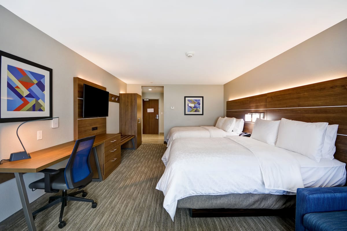A hotel room with a desk, two beds, a TV, and artwork on the walls.
