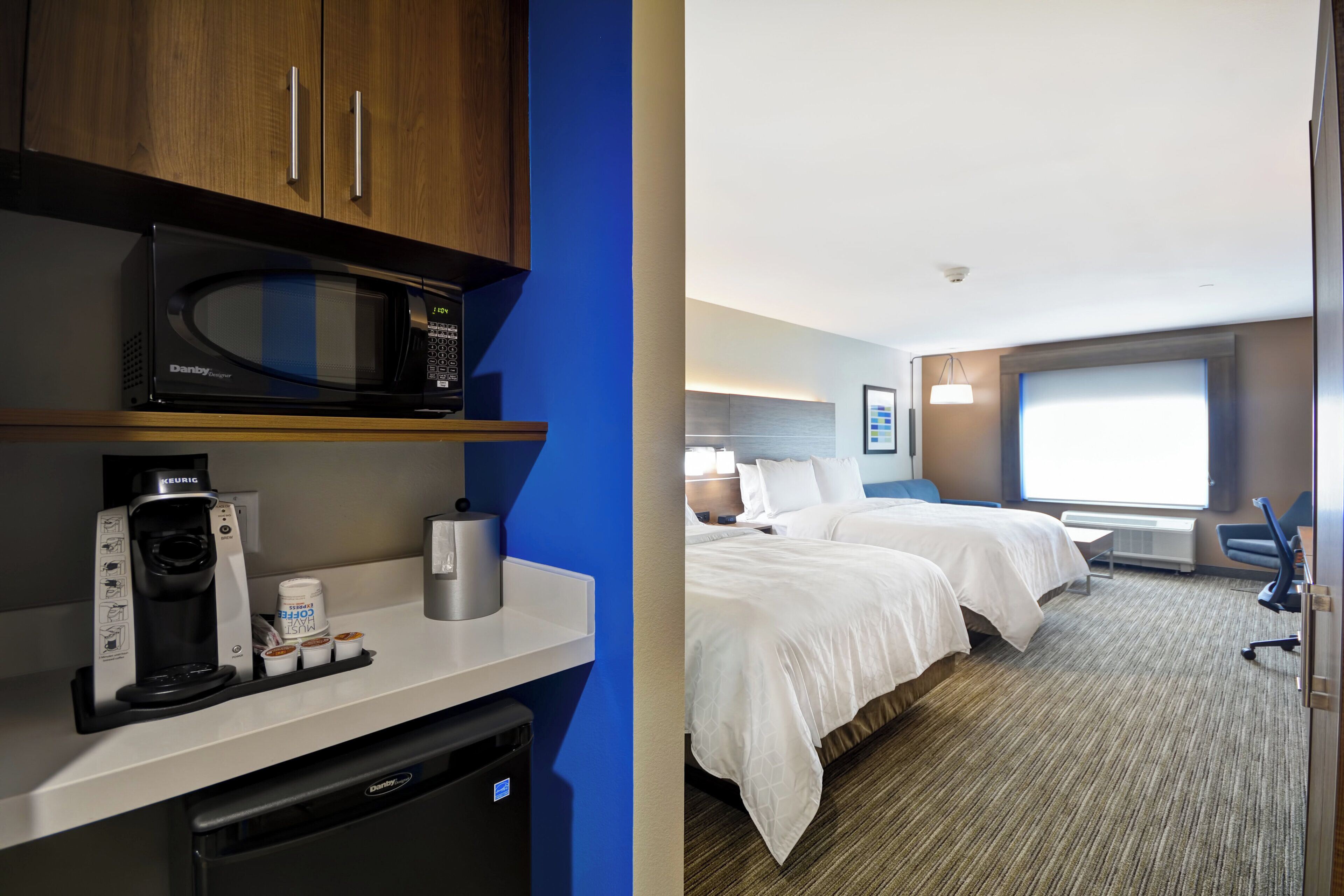 A hotel room with a microwave, coffee maker, and a minibar. There are two beds with white linens and a large window.