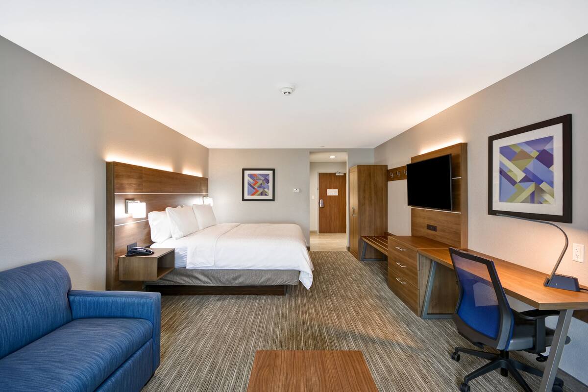 A hotel room with a bed, a desk, a chair, a TV, and a couch.