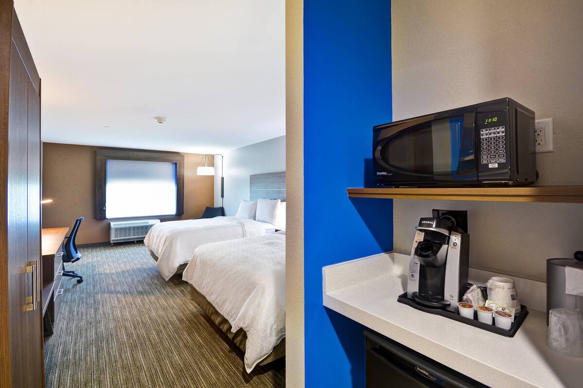 A hotel room with two beds, a desk, a chair, a microwave, and a coffee maker.