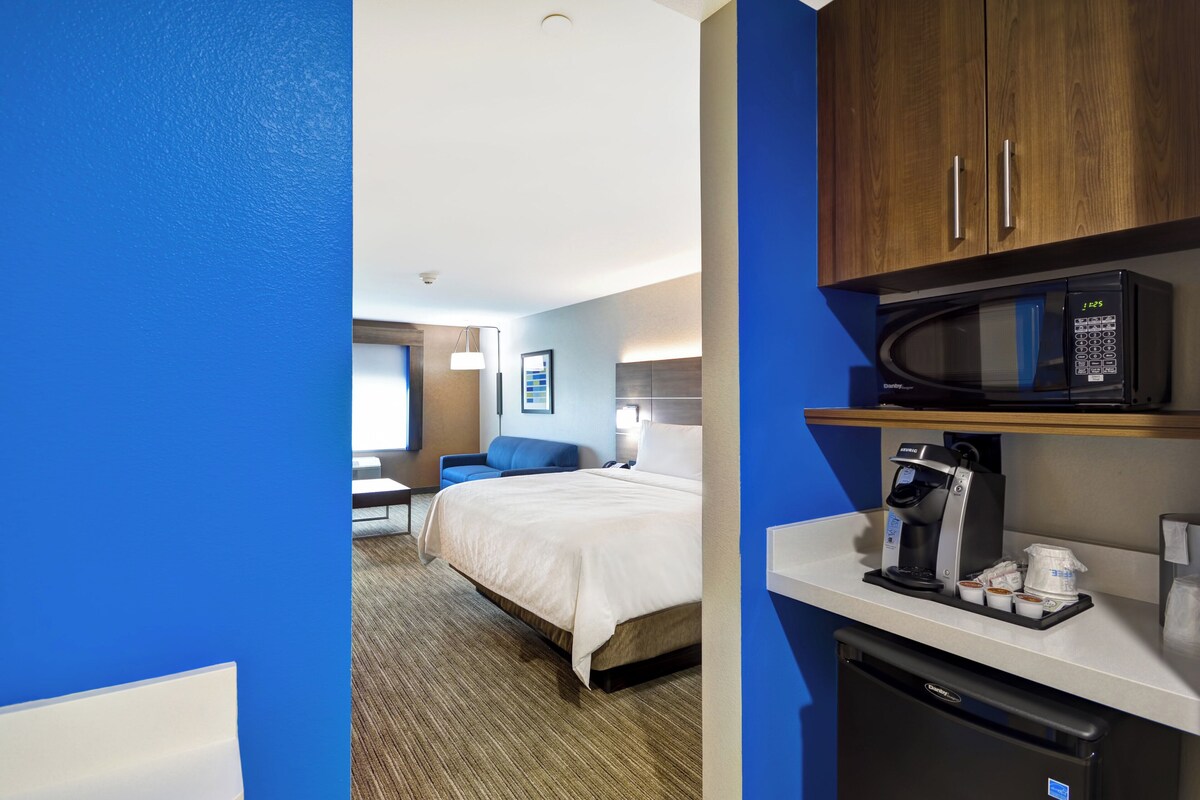 A hotel room with a bed, a desk, a microwave, a coffee maker, and a refrigerator.