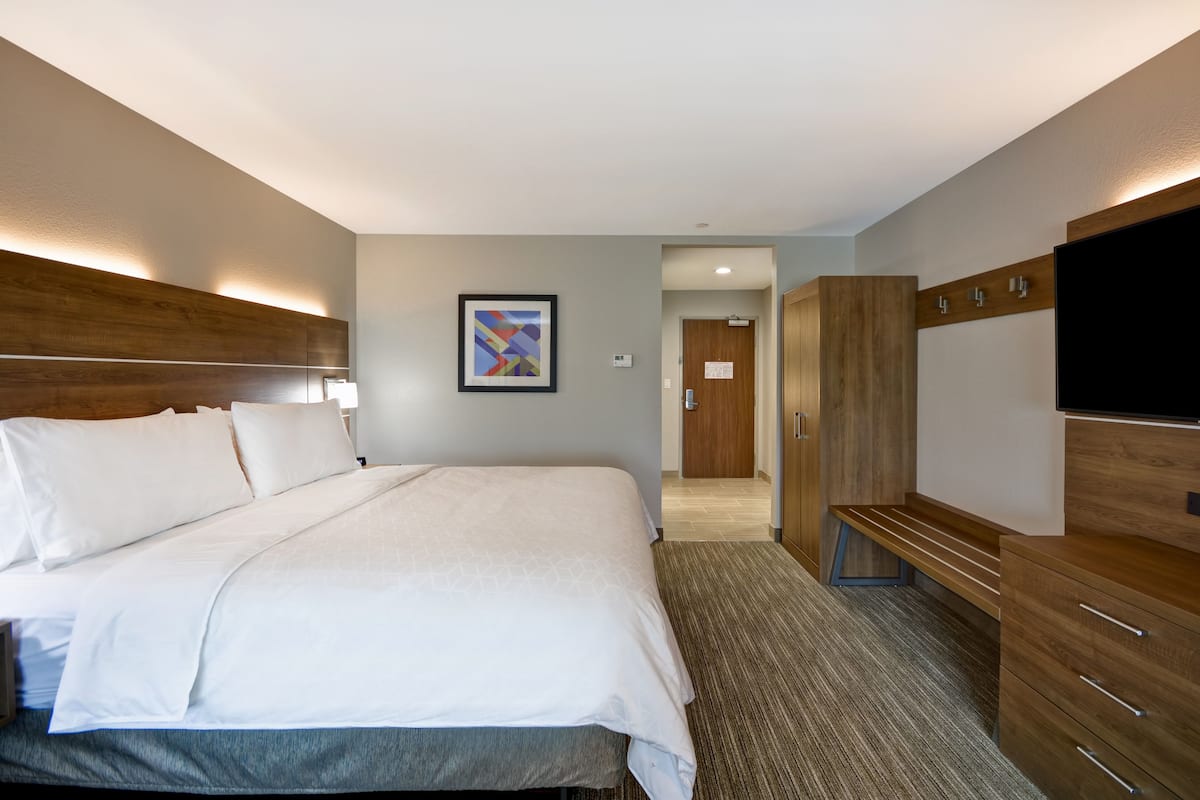 A hotel room with a large bed, a flat-screen TV, wooden furniture, and a framed picture on the wall.