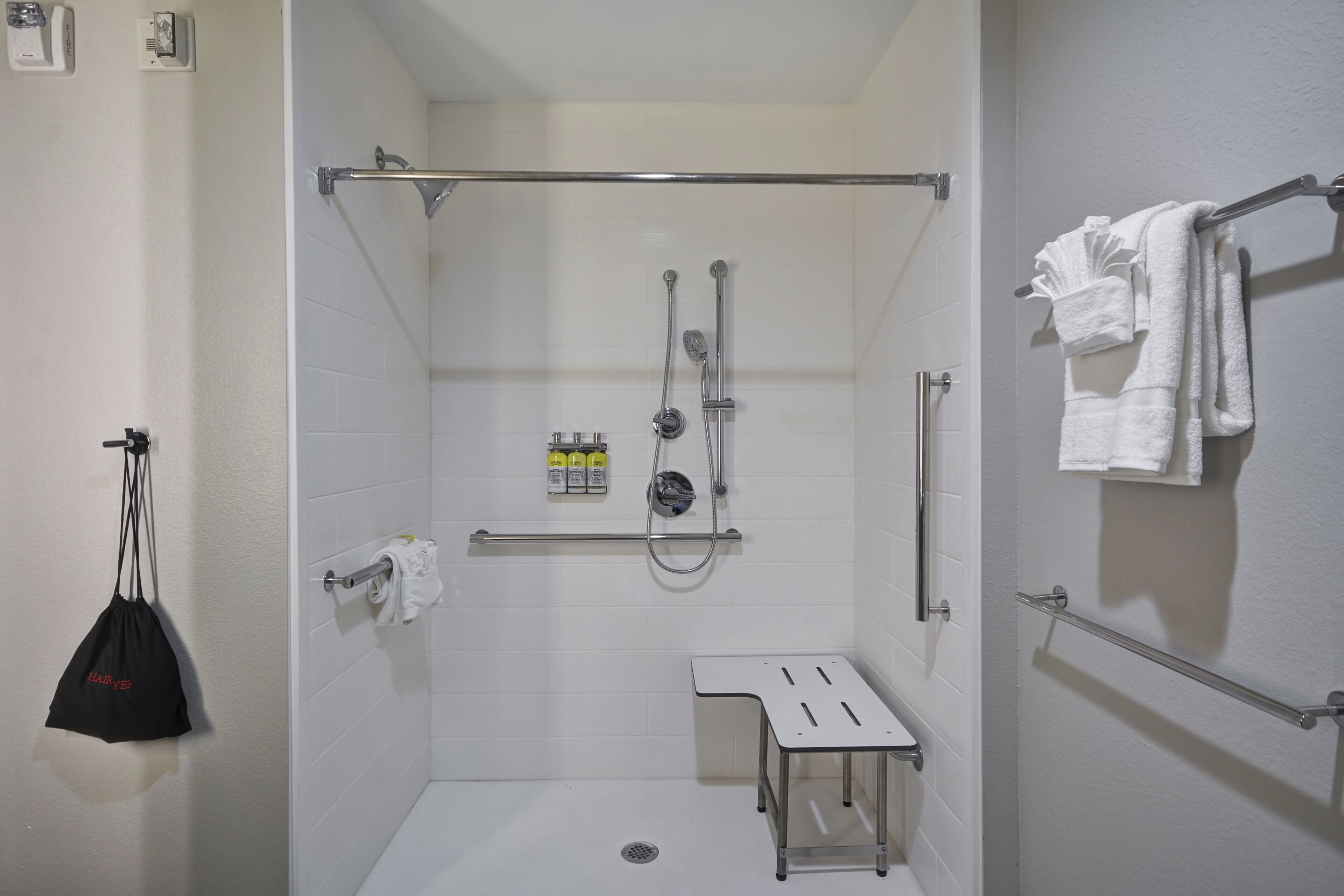 A shower stall with a handheld showerhead, a handheld shower attachment, and a small step stool.