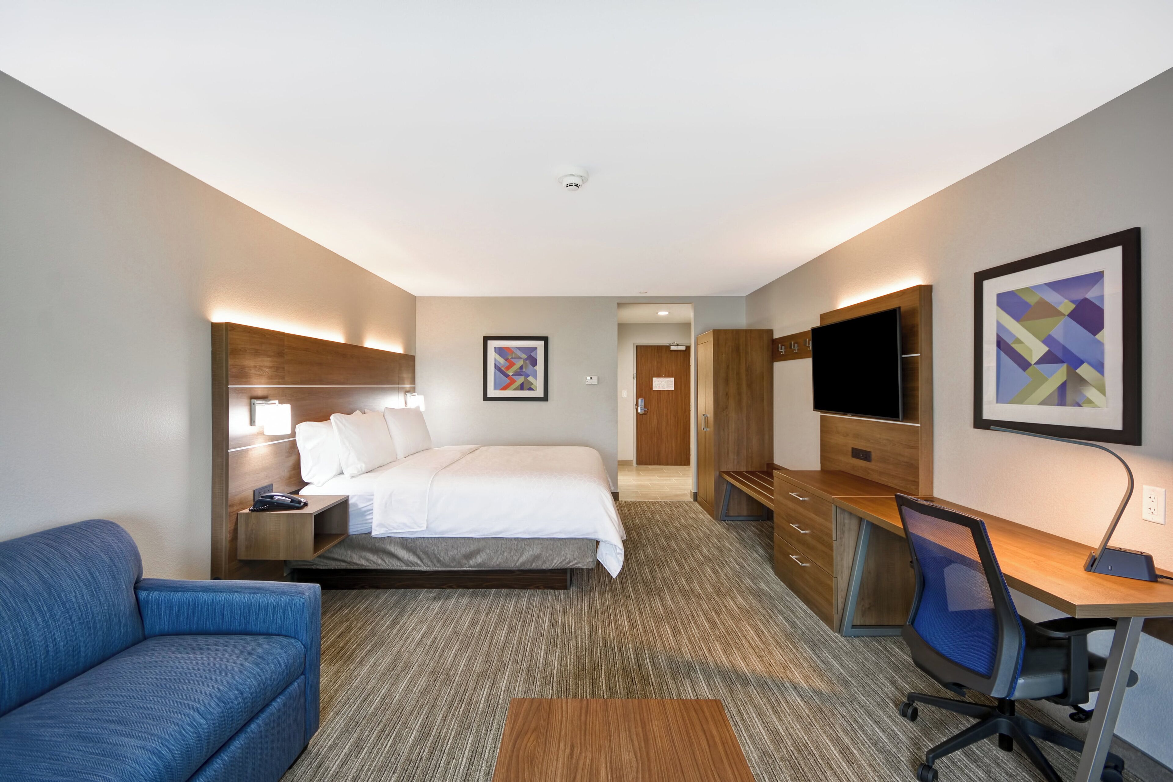 A hotel room with a bed, a desk, a chair, a TV, and a sofa.
