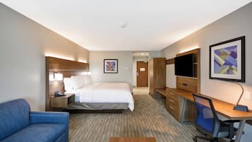 A hotel room with a bed, a desk, a chair, a TV, and a sofa.